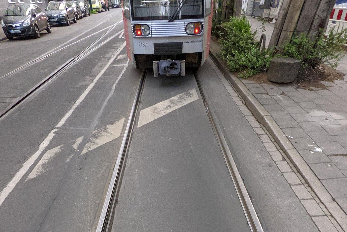 Das Bild zeigt einen Radfahrer, welcher zwischen den Straßenbahnschienen fährt. Davor ist eine Straßebahn, welche an einer Haltestelle hält
