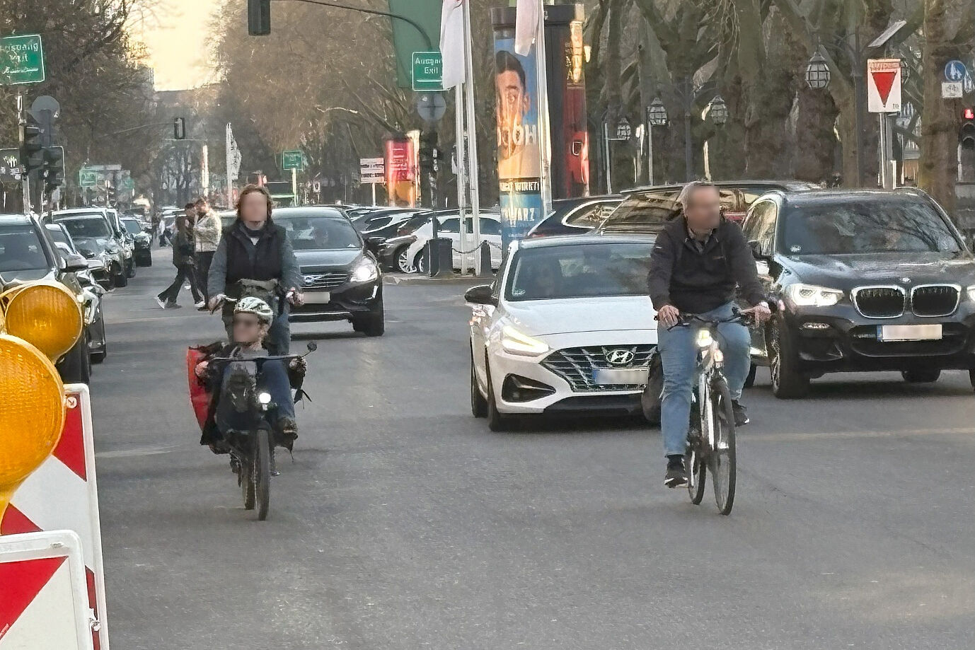 Das Bild zeigt die Königsallee im aktuellen Zustand. Es ist zu sehen, wie Radfahrende und Autofahrer gemeinsam auf der Fahrbahn unterwegs sind.