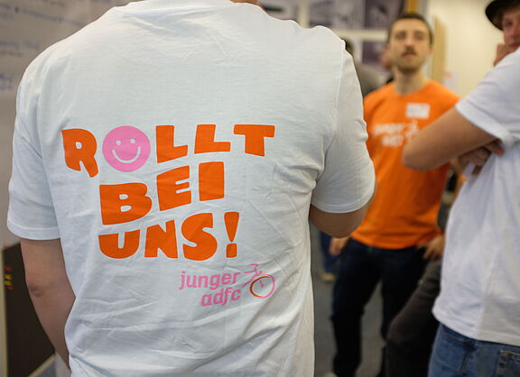Ein Mensch mit einem T-Shirt, auf dem hinten der Spruch "Rollt bei uns!" steht.