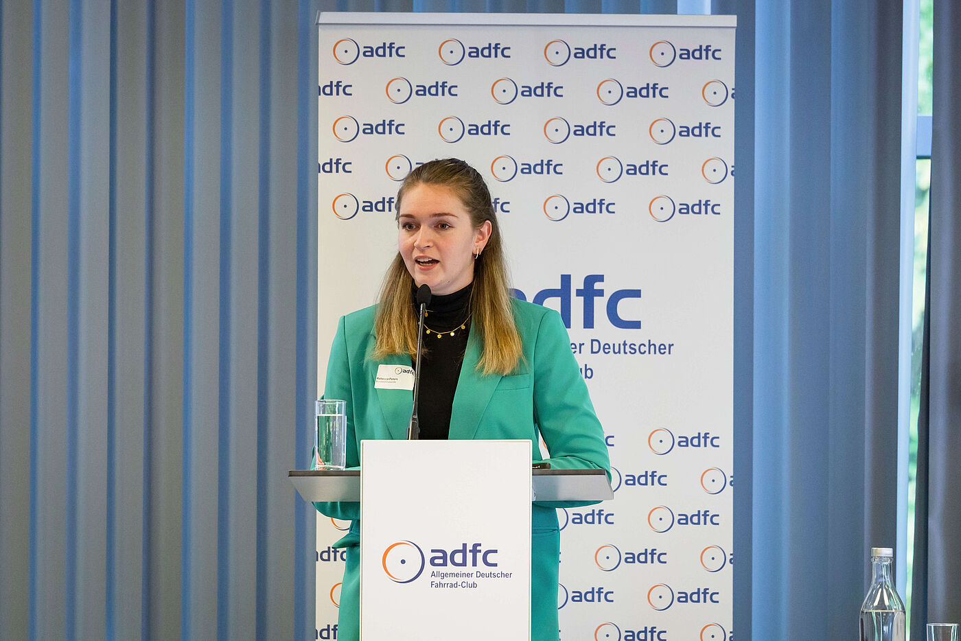 Rebecca Peters steht auf der Bühne und spricht ins Mikrofon.